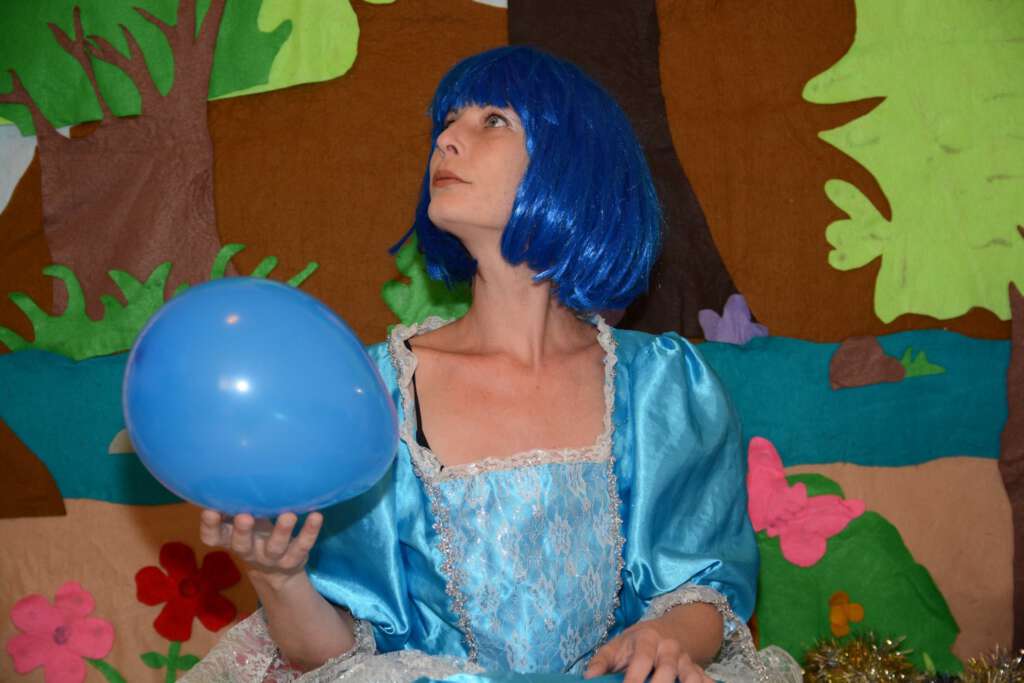 שחקנית עם פאה כחולה ושמלה תכלת מחזיקה בלון כחול